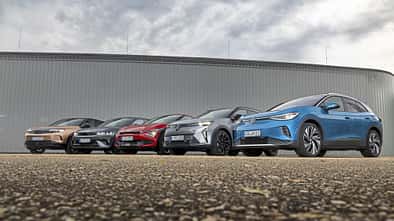 Fünf aktuelle Elektro-SUVs (Hyundai IONIQ 5, VW ID.4 Pro, Opel Grandland, Kia EV6, Renault Scenic E-Tech Electric) nebeneinander vor moderner Industriehalle, fotografiert aus niedriger Perspektive.