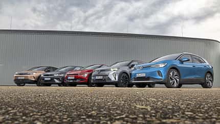 Fünf aktuelle Elektro-SUVs (Hyundai IONIQ 5, VW ID.4 Pro, Opel Grandland, Kia EV6, Renault Scenic E-Tech Electric) nebeneinander vor moderner Industriehalle, fotografiert aus niedriger Perspektive.