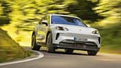 Porsche Cayenne Electric fährt auf einer kurvigen Landstraße durch grüne Landschaft.