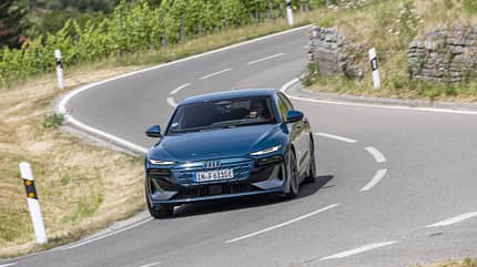 Audi A6 Sportback e-tron f&auml;hrt auf kurviger Landstra&szlig;e durch gr&uuml;ne Landschaft.