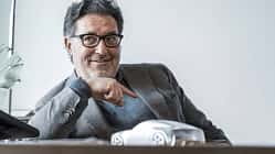 Porträtaufnahme einer Person im Sakko an einem Schreibtisch mit einem Automodell im Vordergrund.