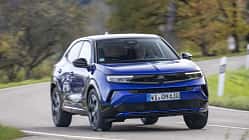 Opel Mokka Hybrid, Hybrid-SUV, Opel, Straße, Kompakt-SUV, Hybridantrieb, Fahrzeug, Automobil, Landstraße, Fahrdynamik Opel Mokka Hybrid fährt auf einer Landstraße durch eine herbstliche Landschaft.