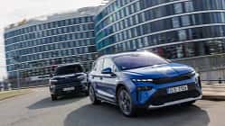 Zwei Elektro-SUVs, Kia EV3 und Skoda Elroq, fahren nebeneinander auf einer städtischen Straße vor modernen Bürogebäuden.