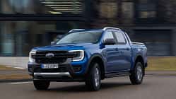 Ford Ranger PHEV 2.3L EcoBoost fährt auf einer Straße, blauer Pickup, Front- und Seitenansicht, Tageslicht.