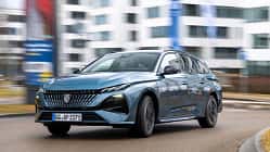 Peugeot e-308 SW 156 PS fährt auf einer städtischen Straße vor modernen Gebäuden.