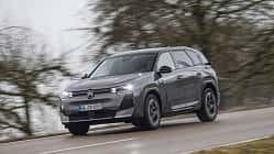 Citroen e-C5 Aircross fährt auf nasser Landstraße, Seitenansicht, grauer SUV, Bäume im Hintergrund.