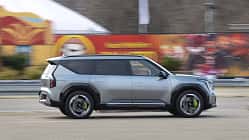 Kia EV9 GT (6 Sitzer) fährt in der Stadt, Seitenansicht, silberner Elektro-SUV vor urbanem Hintergrund.