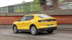 Ford Capri Extended Range 79kWh, Ford Capri, Elektro-SUV, 79kWh Batterie, Straßenfahrt, 2024, Ford, Elektroauto, Crossover, Automobil Gelber Ford Capri Extended Range 79kWh fährt auf einer Straße, fotografiert von hinten in Bewegung.