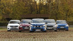 Fünf Kleinwagen-Modelle (Mitsubishi Colt, Dacia Sandero, Opel Corsa, Skoda Fabia, Hyundai i20) nebeneinander auf einem Parkplatz in herbstlicher Umgebung, frontal fotografiert.