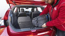 Hyundai i20 T-GDI Kofferraum mit umgeklappter Rückbank, Person lädt Tasche ein.