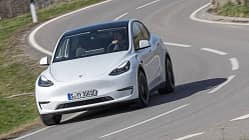 Tesla Model Y, Dauertest, Elektro-SUV, Tesla, Elektroauto, Langzeittest, Straßenfahrt, Fahrbericht, Automobil, E-Mobilität Tesla Model Y in weiß auf einer kurvigen Landstraße während eines Dauertests, frontal fotografiert.