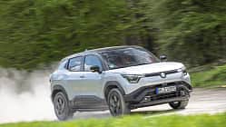 Suzuki e-Vitara eAxle, Suzuki SUV, Elektro-SUV, eAxle, Crossover, Elektroantrieb, 2024, Allradantrieb, Automobil, Fahrdynamik Suzuki e-Vitara eAxle SUV fährt dynamisch auf einer Landstraße, im Hintergrund grüne Vegetation.