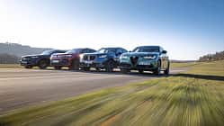 Vier Mittelklasse-SUVs – Mercedes GLC 220d 4Matic, BMW X3 xDrive 20d, Alfa Romeo Stelvio 2.0 Diesel und VW Tiguan 2.0 TDI – fahren nebeneinander auf einer Landstraße.