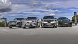 Vier Elektro-SUVs – Audi Q6 SUV e-tron quattro, BMW iX3 50 xDrive, Mercedes GLC 400 4matic EQ und Porsche Macan 4S – nebeneinander auf einer offenen Fläche, fotografiert aus niedriger Perspektive, mit Himmel und Wolken im Hintergrund.