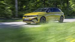 Opel Astra PHEV, Plug-in-Hybrid, Kompaktklasse, Opel, Straße, Fahrzeug, Hybridantrieb, Limousine, Automobil, Fahrt Opel Astra PHEV in Gelb fährt auf einer Landstraße durch grüne, bewaldete Umgebung. Das Fahrzeug ist im Profil zu sehen, mit sichtbarem Fahrer und dynamischer Bewegungsunschärfe im Vordergrund.