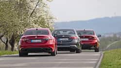 Drei Limousinen, Alfa Romeo Giulia 2.2 Diesel Q4, BMW 320d und Mercedes C 220d, fahren auf einer Landstraße. Die Fahrzeuge sind von hinten zu sehen, umgeben von blühenden Bäumen und einer hügeligen Landschaft.
