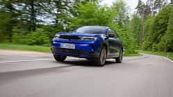 Opel Mokka, Kompakt-SUV, Elektroauto, Straßenfahrt, Fahrdynamik, Opel, SUV, Automobil, Landstraße, Froschperspektive Opel Mokka fährt auf einer Landstraße durch grüne, bewaldete Umgebung. Das Fahrzeug ist in Bewegung und aus der Froschperspektive aufgenommen.