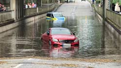 07/2026, Wasserdurchfahrt Panne Polizei Ein Polizeiauto und ein roter Mercedes stehen hüfthoch in einer überschwemmten Straßensenke