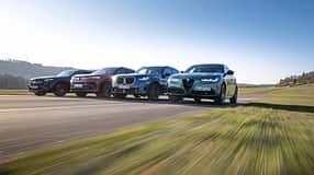Vier Mittelklasse-SUVs – Mercedes GLC 220d 4Matic, BMW X3 xDrive 20d, Alfa Romeo Stelvio 2.0 Diesel und VW Tiguan 2.0 TDI – fahren nebeneinander auf einer Landstraße.