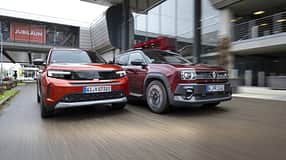 Opel Frontera Electric und Renault 4 E-Tech 150 fahren nebeneinander auf einer Straße vor moderner Architektur.