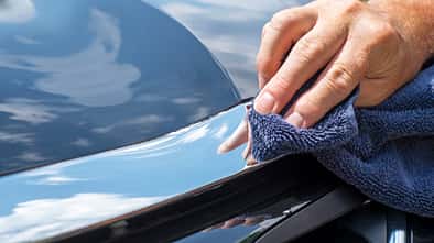 Close-up man polishing chrome trim on new black car
