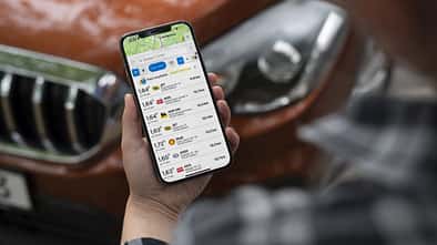Mann schaut auf Smartphone vor Auto stehend.