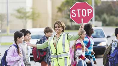 Schulkinder werden von Frau über die Straße geleitet