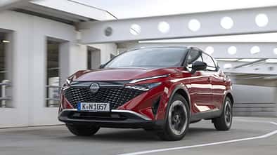 Nissan Qashqai e-Power 156 in Rot, fahrend in urbaner Umgebung, Front- und Seitenansicht.