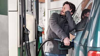 Young man refueling his vehicle while looking worried at the high gas prices.