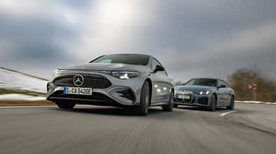 BMW i4 xDrive40 Gran Coupe und Mercedes CLA 350 EQ fahren auf einer Landstraße bei winterlichen Bedingungen.