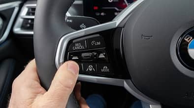 Detailaufnahme des Multifunktionslenkrads eines BMW i4 xDrive40 Gran Coupe, Fokus auf Bedientasten für Assistenzsysteme.