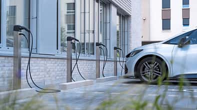 Mehrere MAHLE charge BIG und Smallbox Ladesäulen für Elektrofahrzeuge vor einem modernen Gebäude, ein Elektroauto ist angeschlossen.