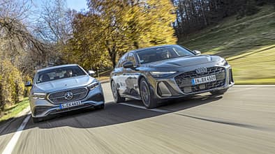 Audi A6 TFSI quattro und Mercedes E450 4matic fahren nebeneinander auf einer Landstraße im Herbst.