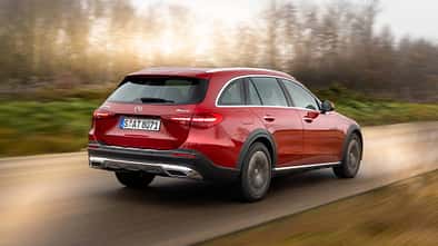 Mercedes C220d 4matic All-Terrain in Rot fährt auf einer Landstraße, fotografiert von schräg hinten, unscharfer Hintergrund.