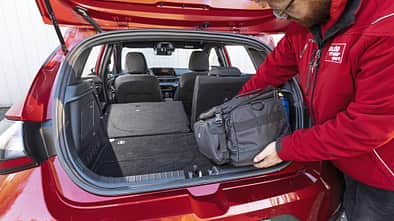 Hyundai i20 T-GDI Kofferraum mit umgeklappter Rückbank, Person lädt Tasche ein.
