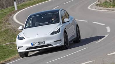 Tesla Model Y in weiß auf einer kurvigen Landstraße während eines Dauertests, frontal fotografiert.