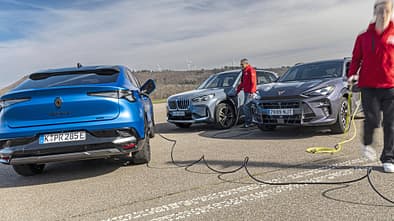 Renault Rafale Hyper Hybrid E-Tech, BMW X1 xDrive 30e, Cupra Terramar VZ e-Hybrid, Plug-in-Hybrid, SUV, Ladeszene, Elektromobilität, Vergleichstest, Ladestation, Gruppenaufnahme Drei Plug-in-Hybrid-SUVs (Renault Rafale Hyper Hybrid E-Tech, BMW X1 xDrive 30e, Cupra Terramar VZ e-Hybrid) werden auf einem Parkplatz geladen. Zwei Personen in roten Jacken hantieren mit Ladekabeln.