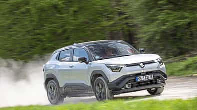 Suzuki e-Vitara eAxle SUV fährt dynamisch auf einer Landstraße, im Hintergrund grüne Vegetation.