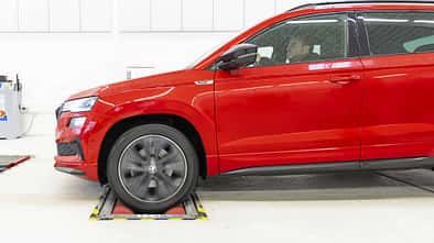 Rotes Skoda Karoq SUV, Seitenansicht, auf Rollenprüfstand in heller Werkstattumgebung, Fahrer am Steuer.