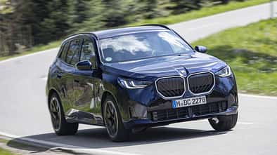 BMW X3 20 xDrive fährt auf einer Landstraße durch eine Kurve. Das SUV ist in dunkler Lackierung zu sehen.