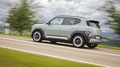 Der Dateiname nennt das Modell "Kia EV2 RG26". Das Bild zeigt einen Kia EV2 RG26 als SUV in Seitenansicht auf einer Landstraße in Bewegung. Die Aufnahme ist dynamisch, mit unscharfem Hintergrund und klar erkennbarem Fahrzeug.