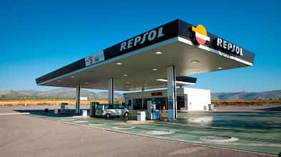 Eine einsame Tankstelle der Marke Repsol in Spanien vor einer Bergkulisse mit blauem Himmel und einem silberfarbenen Fahrzeug an einer der Tanksäulen