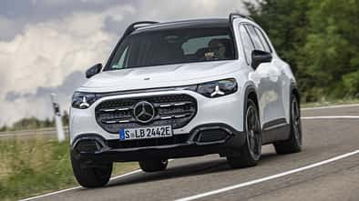Mercedes GLB 250+ auf Landstraße, Frontansicht, weißes SUV, dynamische Kurvenfahrt, Tageslicht.