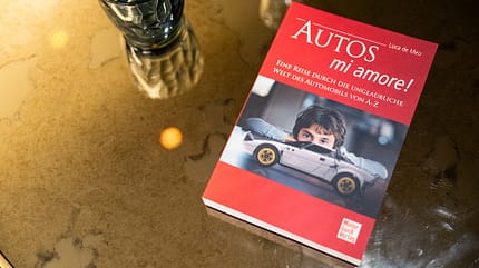 Buchcover 'Autos mi amore!' von Luca de Meo auf einem Glastisch mit Wasserglas und Karaffe, fotografiert im Publicis Drugstore in Paris im Juli 2025.