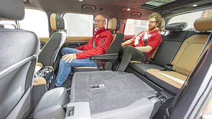 Land Rover Defender 130 D250, SUV-Innenraum, Siebensitzer, Rücksitzbank, Innenraum, Laderaum, Sitzkomfort, Geländewagen, 2024, Fahrzeuginterieur Innenraumaufnahme eines Land Rover Defender 130 D250 mit zwei Personen auf der zweiten und dritten Sitzreihe. Die Rücksitze sind teilweise umgeklappt, um die Variabilität des Laderaums zu zeigen.