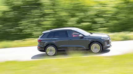 Audi Q6 SUV e-tron quattro fährt auf einer Landstraße, Seitenansicht, grüne Umgebung, Bewegungseffekt.