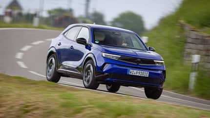 Opel Mokka, SUV, Kompakt-SUV, Straßenfahrt, Opel, Elektroauto, Fahrdynamik, Crossover, Automobil, Fahrzeug Opel Mokka in blauer Lackierung fährt dynamisch auf einer Landstraße durch eine Kurve.