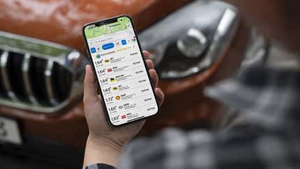 Mann schaut auf Smartphone vor Auto stehend.