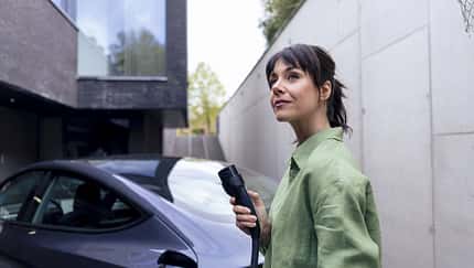 Mature businesswoman holding electric plug and standing near car in parking