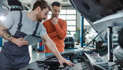 Kunde und Kfz-Techniker sprechen in einer Werkstatt über das Autoproblem